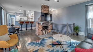 Een moderne woonkamer met een open haard, een plafondventilator en een eethoek met barstoelen.