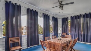Een overdekt terras met een houten tafel en stoelen, witte muren en donkere gordijnen.