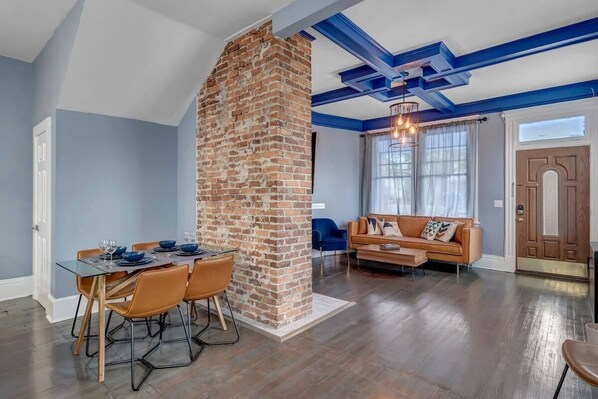 Amplia sala de estar con chimenea de ladrillo, una mesa de comedor con sillas, un sofá y un ventanal con cortinas.