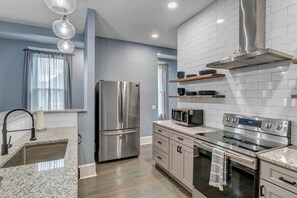 Una cocina moderna con electrodomésticos de acero inoxidable, encimeras de granito y salpicadero de azulejos blancos.