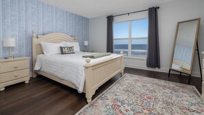 A bedroom with a bed, bedside tables, a mirror, a window with curtains, and a patterned rug.