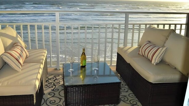 A balcony with a view of the ocean, featuring two sofas and a table with a bottle and glasses.