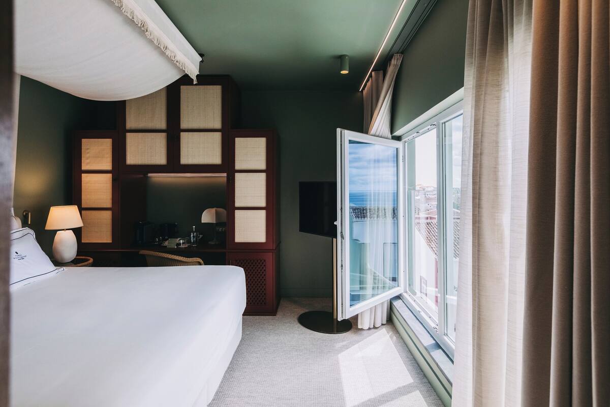 A hotel room with a bed, a desk, a chair, a TV, and a window with curtains.