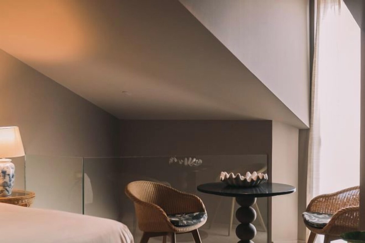 A hotel room with a bed, two wicker chairs, a small round table, and a lamp.