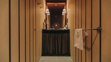 A narrow hallway with wooden paneling, a towel hanging on a metal rack, and two wall-mounted lamps.