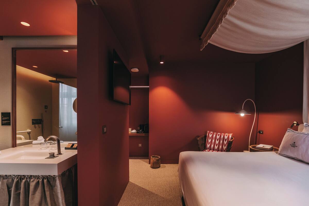 A hotel room with a bed, bedside table, lamp, and a mirror.