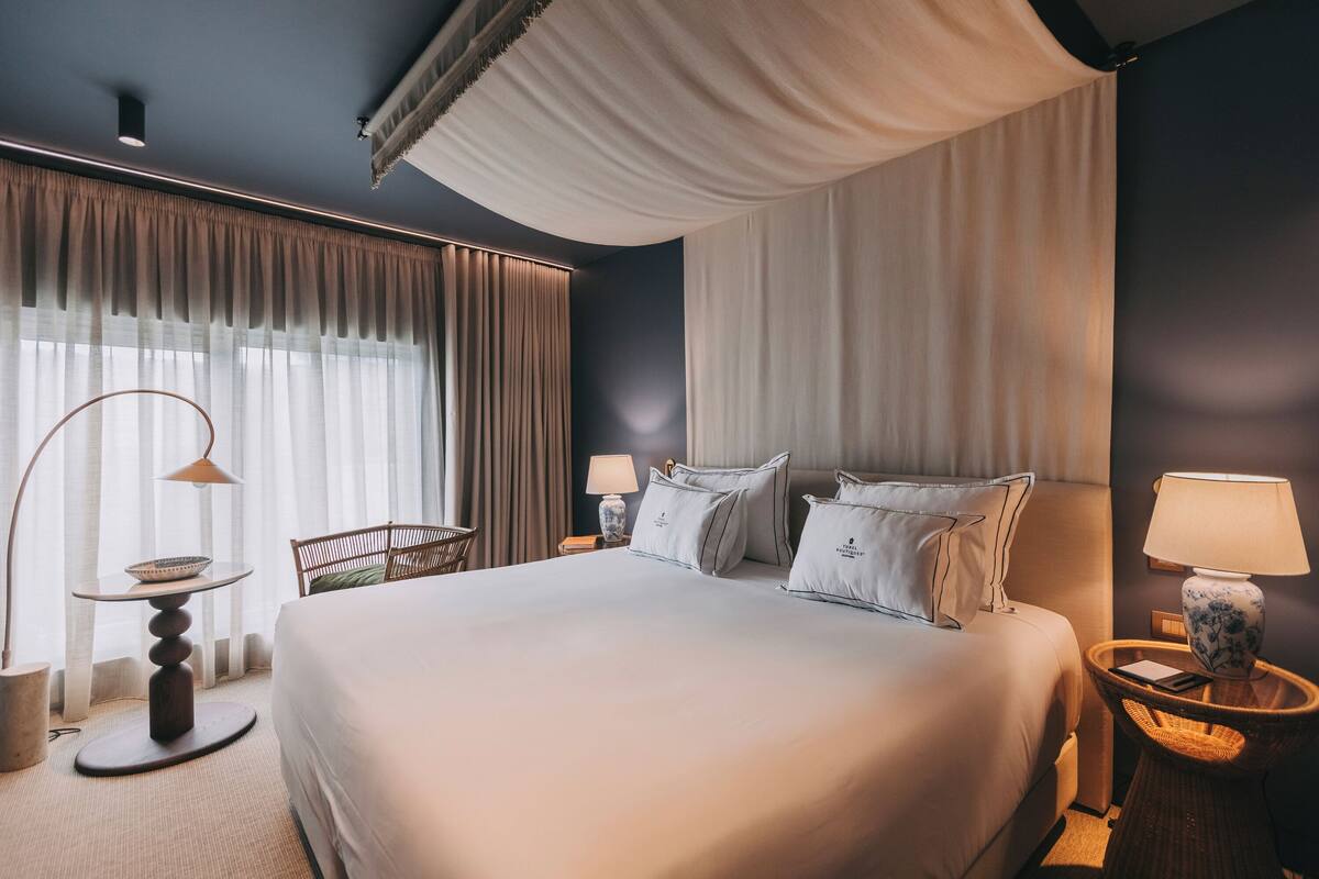 A hotel room with a large bed, two bedside tables with lamps, a chair, and a window with curtains.
