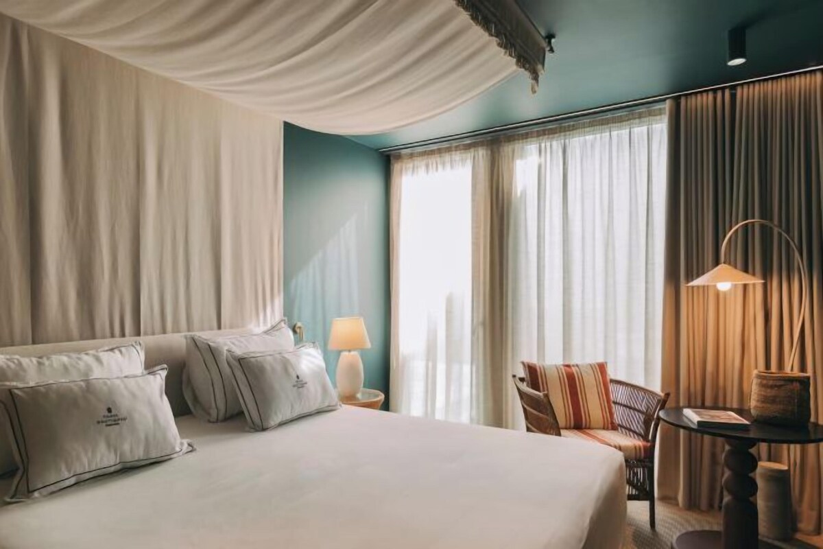A hotel room with a large bed, a chair, a table, and a lamp.