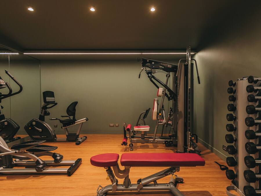 A gym with exercise equipment, a bench, and a wall of dumbbells.