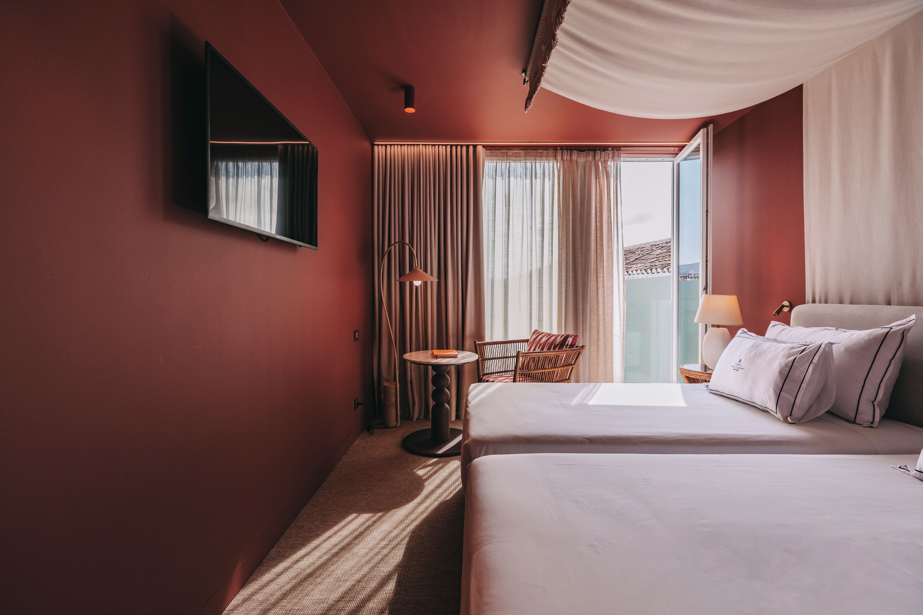 A hotel room with a bed, a chair, a small table, and a window with curtains.
