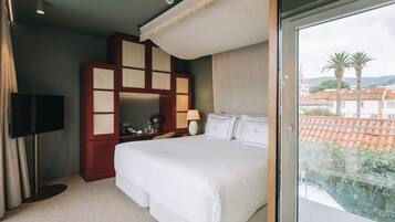 A hotel room with a large bed, a TV, a desk with a lamp, and a view of the city through the window.