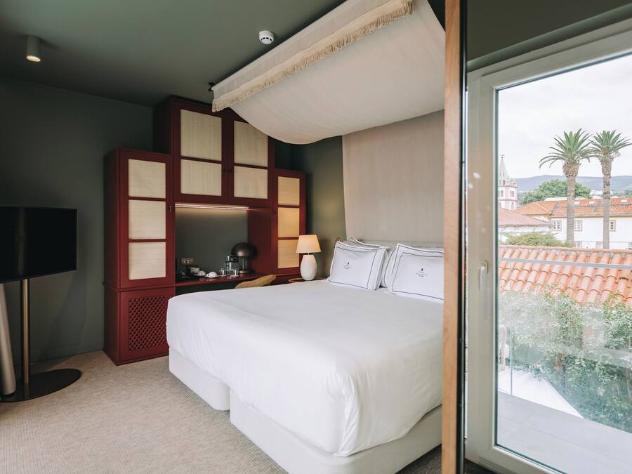 A hotel room with a large bed, a TV, a desk with a lamp, and a view of the city through the window.