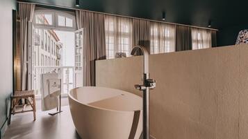 Une salle de bain moderne avec une baignoire sur pieds, un tabouret en bois et une vue sur un immeuble à travers une grande fenêtre.