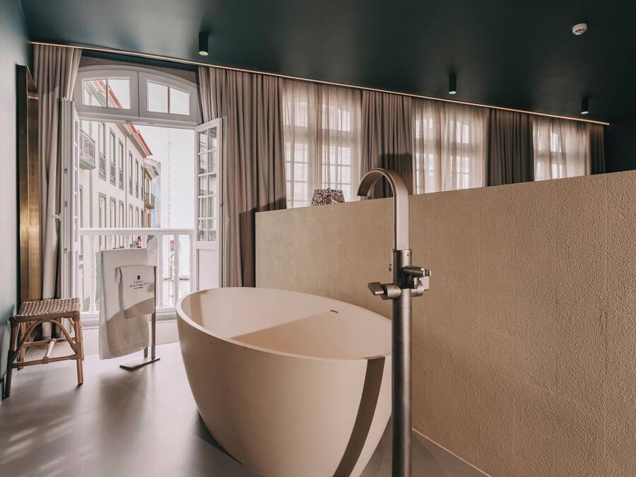 Une salle de bain moderne avec une baignoire sur pieds, un tabouret en bois et une vue sur un immeuble à travers une grande fenêtre.