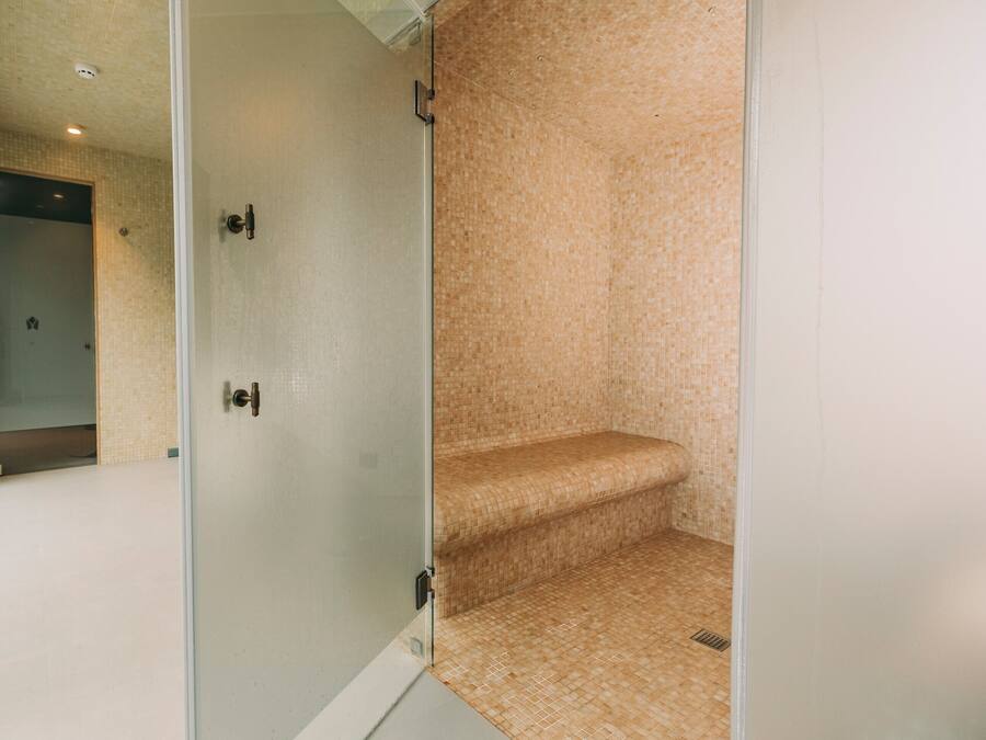 A glass-enclosed shower area with a tiled floor and bench.