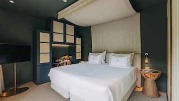 A modern hotel room with a large bed, a television, a desk, and a wicker side table.