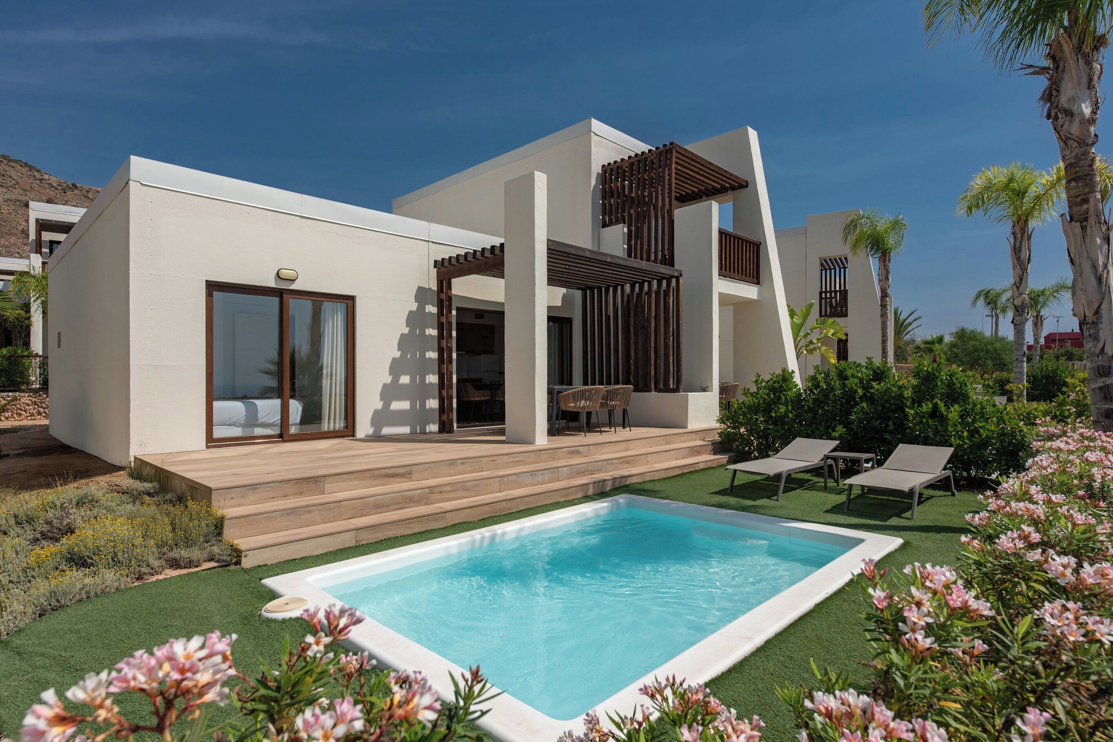 A modern house with a swimming pool, a covered patio, and a garden with flowers and palm trees.