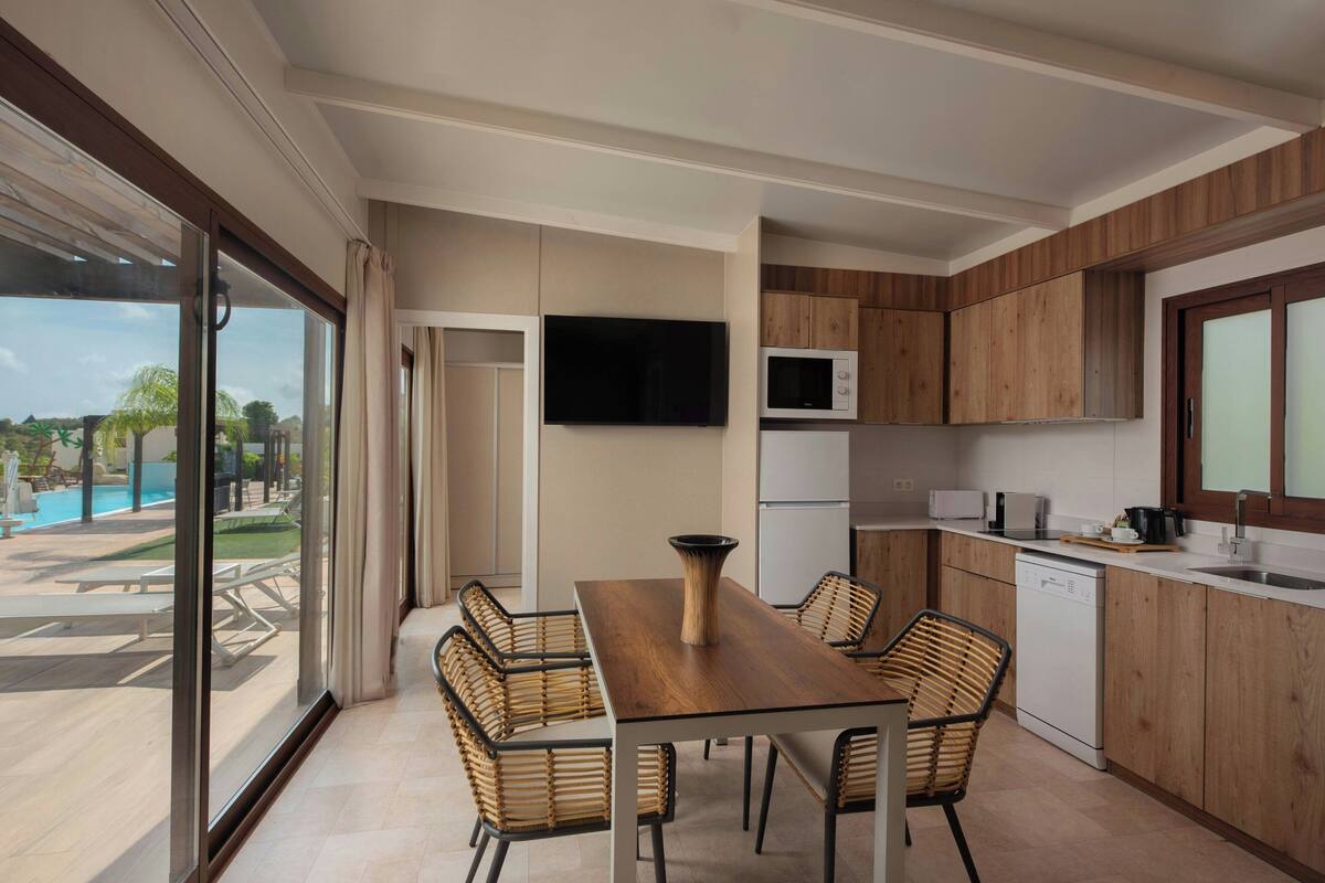 Una cocina moderna con armarios de madera, una mesa de comedor con sillas, un televisor y un lavavajillas.