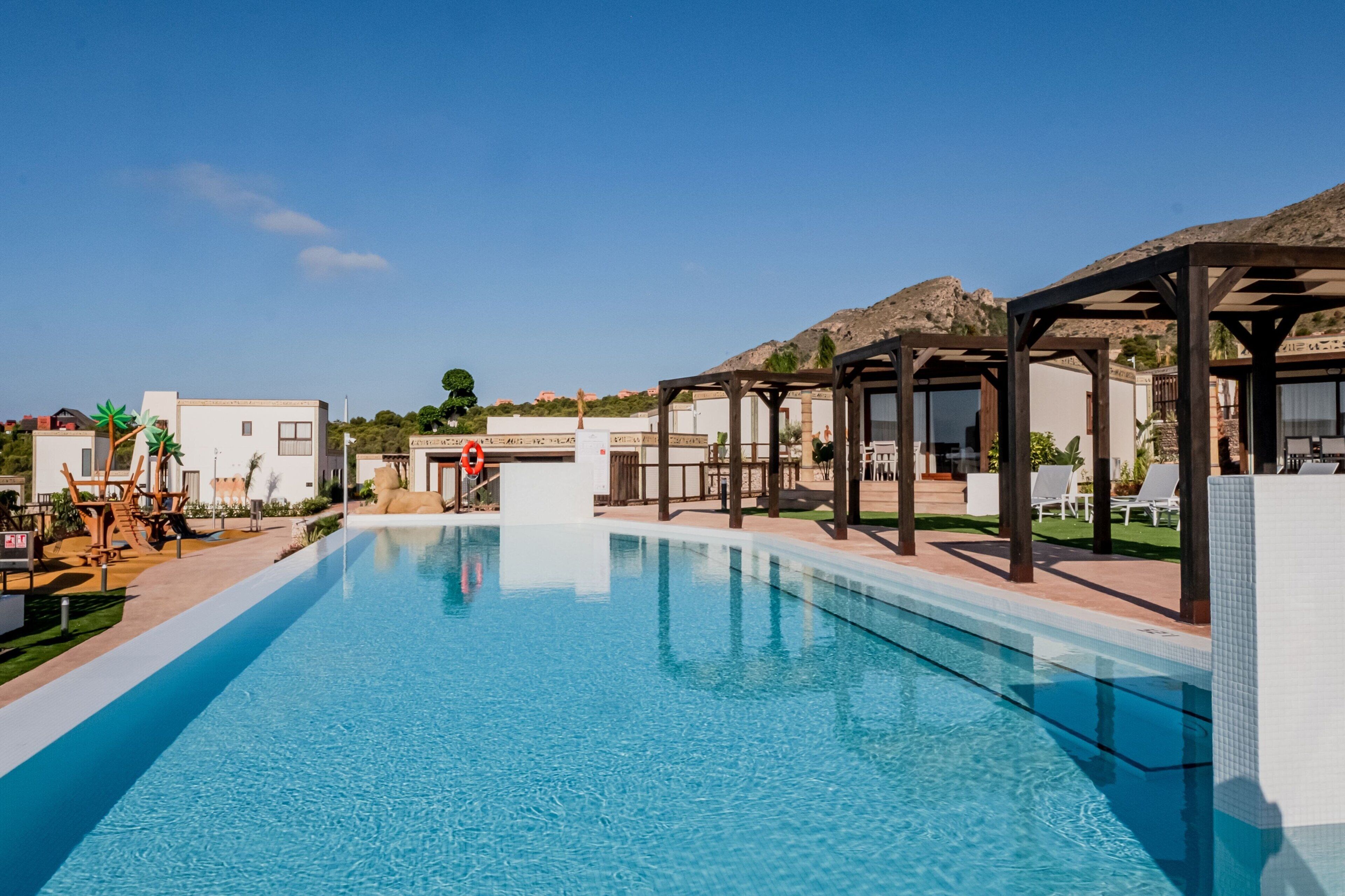 Ein Swimmingpool mit klarem, blauem Wasser, umgeben von Liegestühlen und Sonnenschirmen, mit Blick auf die Landschaft im Hintergrund.
