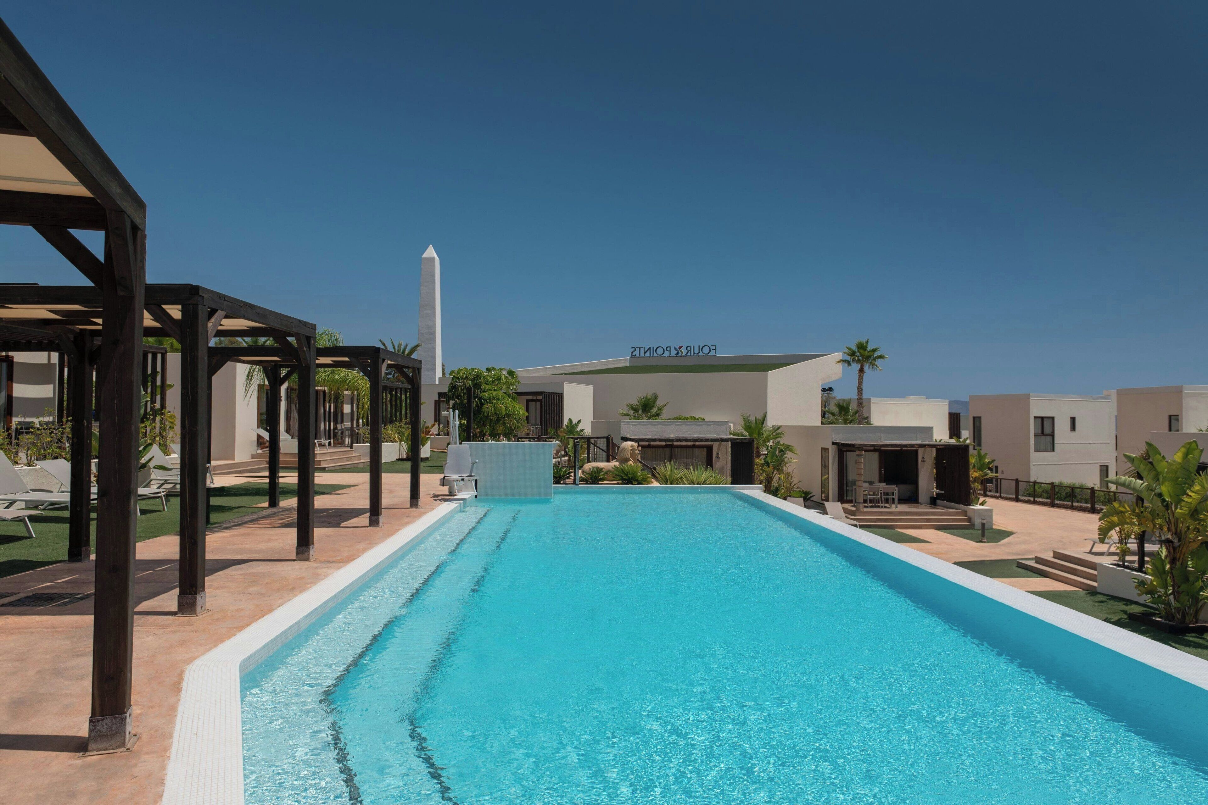 A swimming pool with a clear blue water, surrounded by lounge chairs and a pavilion.