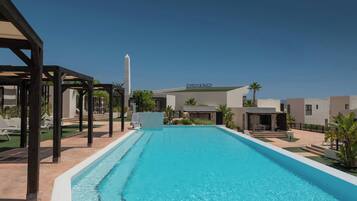 A swimming pool with a clear blue water, surrounded by lounge chairs and a pavilion.