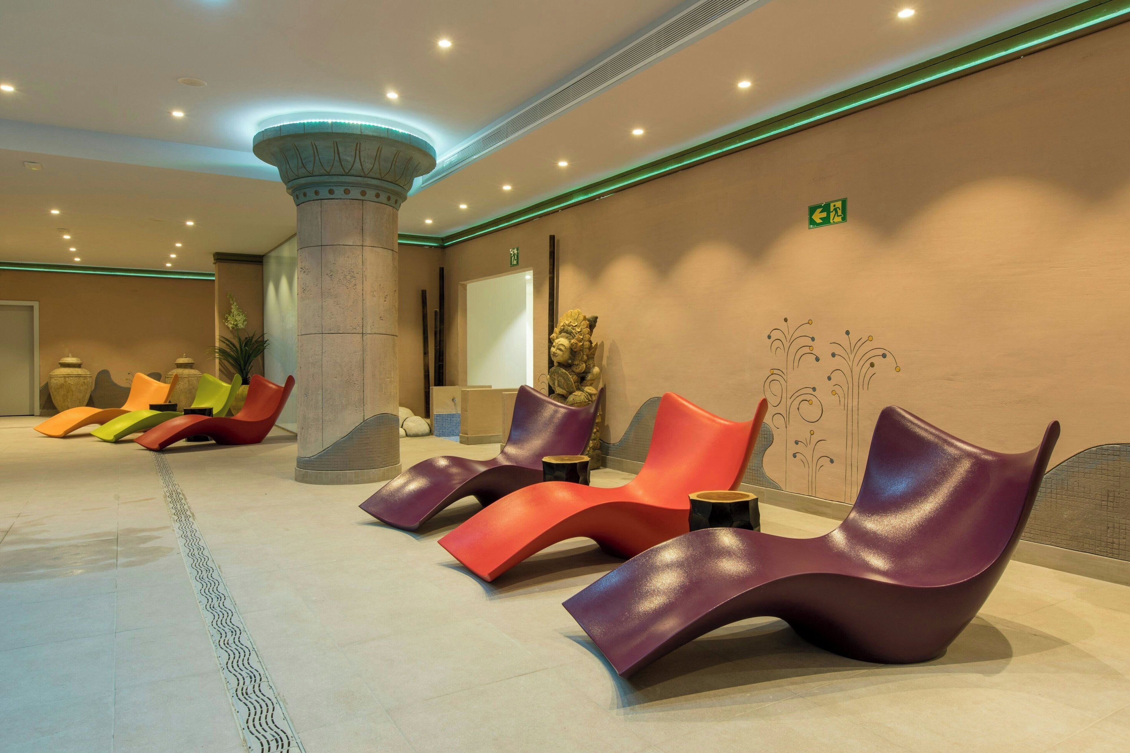 Un lobby moderno con una fila de sillones coloridos, un pilar grande y una pared decorativa.