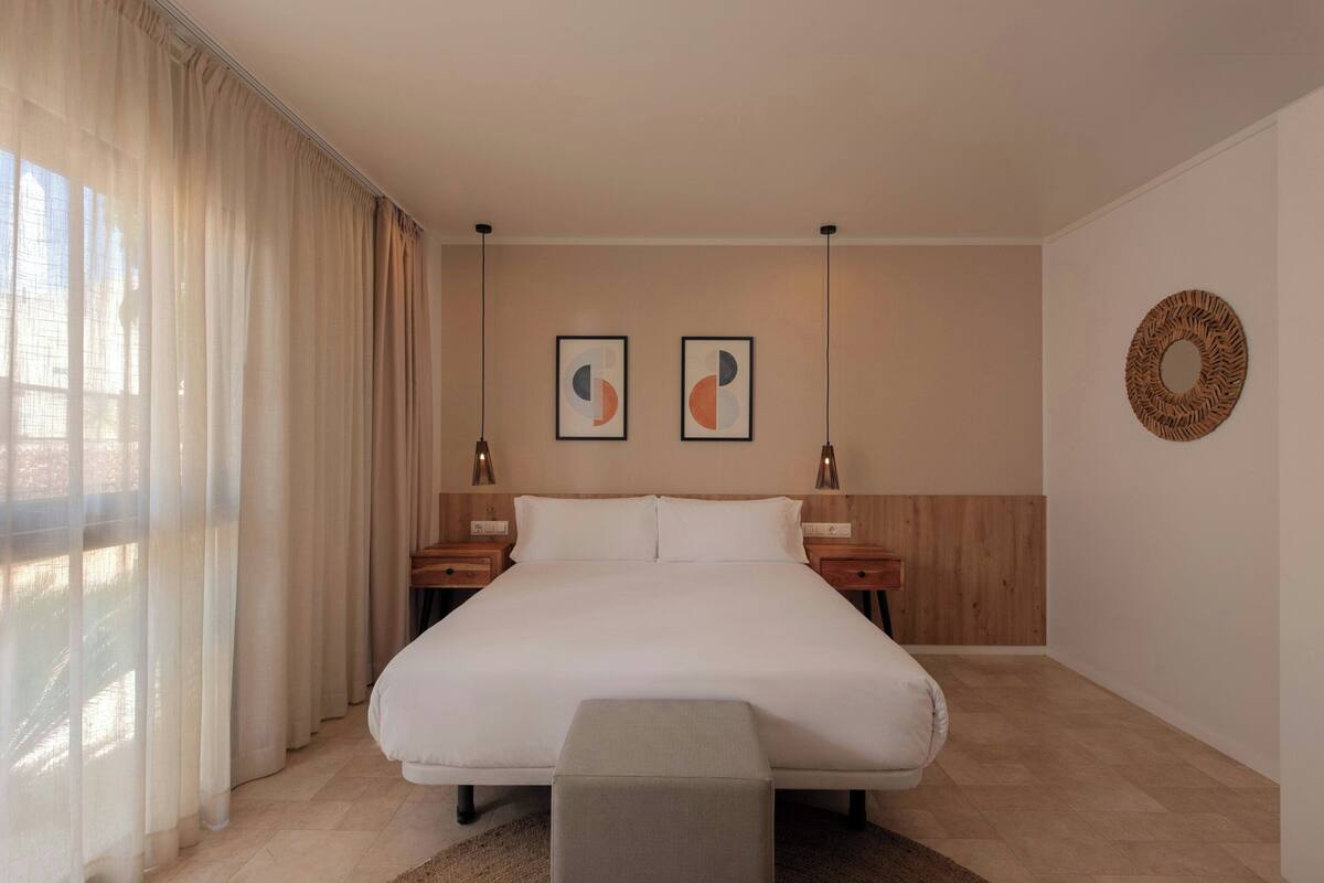 Un dormitorio con una cama grande, dos mesitas de noche, un banco y un adorno en la pared.