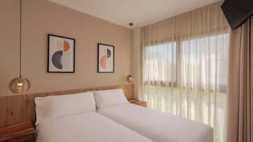 Habitación de hotel con dos camas, cabecera de madera, ventana grande con cortinas translúcidas y dos cuadros abstractos en la pared.