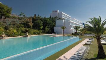 A hotel with a large swimming pool, lounge chairs, and palm trees.