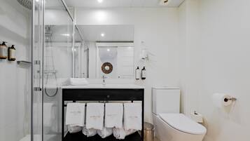 A modern bathroom with a glass-enclosed shower, a white sink with a black countertop, and a toilet.