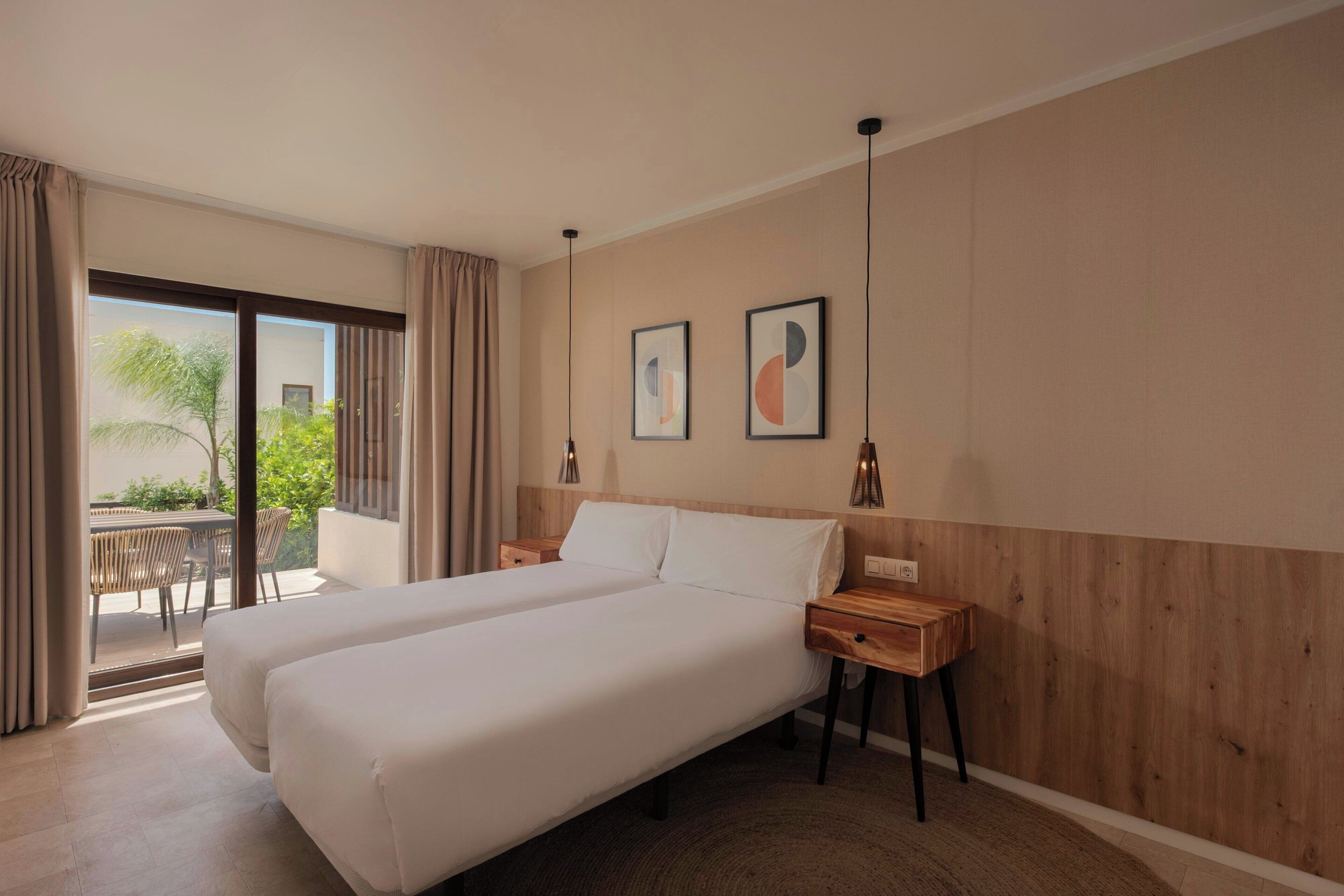 Ein Hotelzimmer mit einem Bett, einem Nachttisch aus Holz und Blick ins Freie.