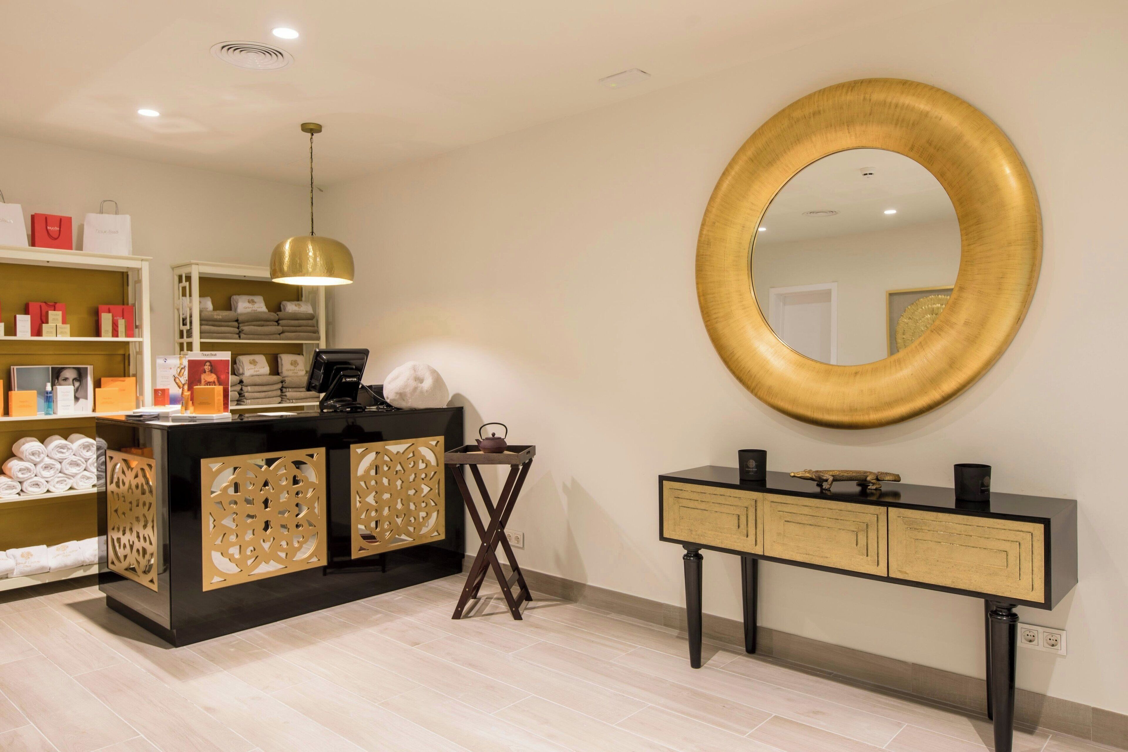Un área de recepción con un mostrador negro, un espejo con marco dorado y un mueble de madera con detalles decorativos cortados.