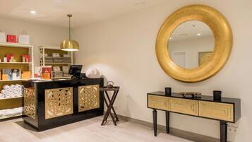 Un área de recepción con un mostrador negro, un espejo con marco dorado y un mueble de madera con detalles decorativos cortados.