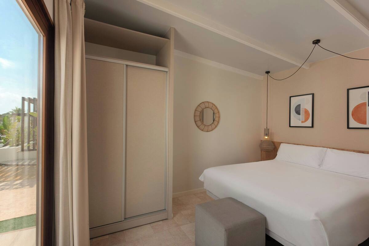 Un dormitorio con una cama grande, un armario, un espejo redondo y cuadros en la pared.