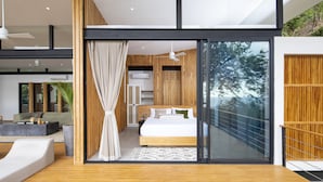 A modern bedroom with a large bed, a glass door leading to a balcony, and a view of trees. - Luxury modern Villa North Santa Teresa Walk To Surf (Santa Teresa Beach)