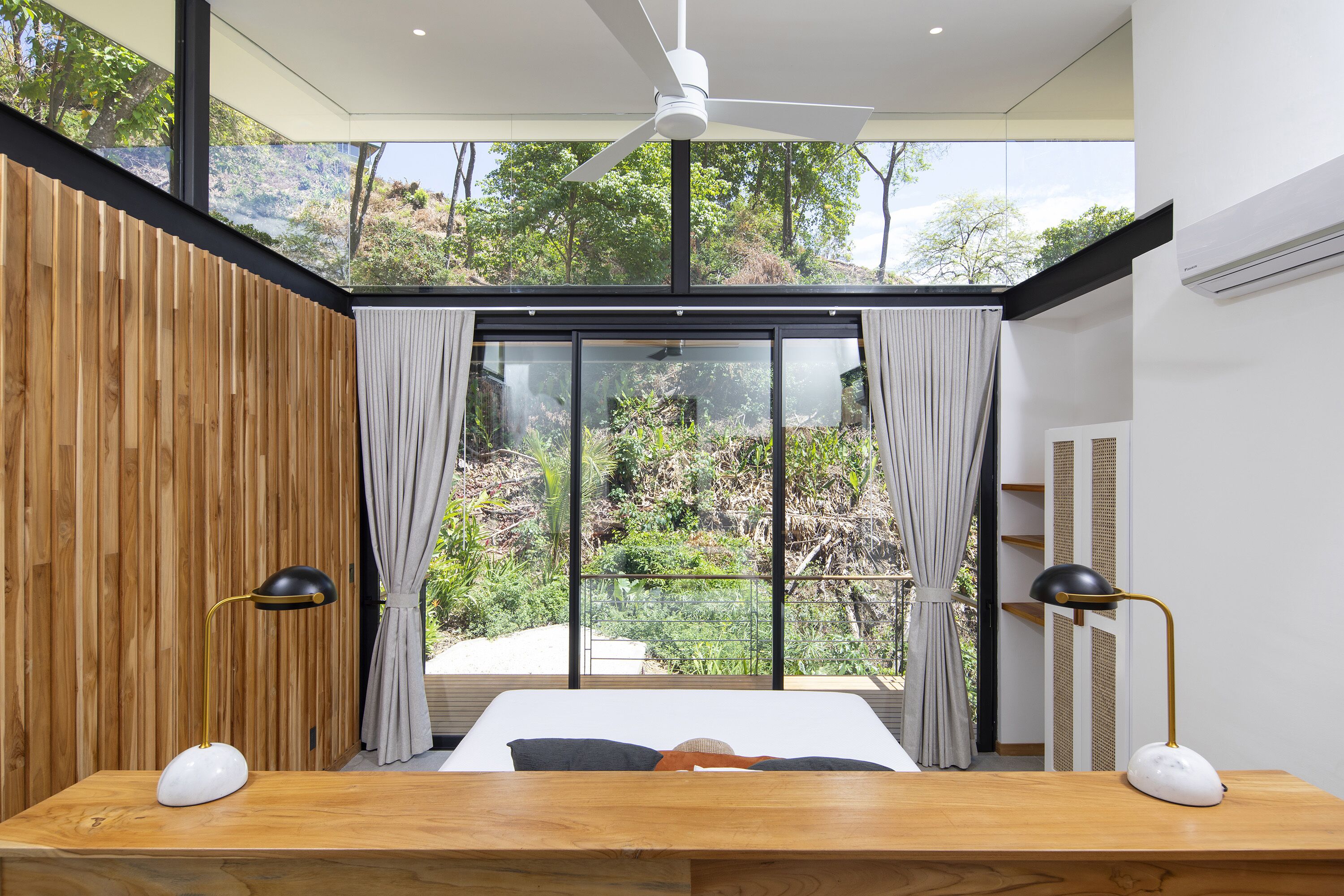A bedroom with a large window, a ceiling fan, and two bedside lamps.