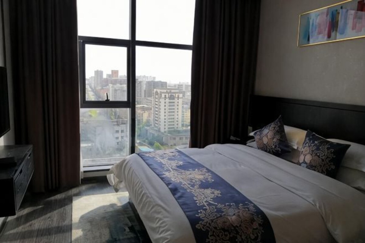 Habitación de hotel con una cama grande, una cómoda y vistas de la ciudad a través de un amplio ventanal.