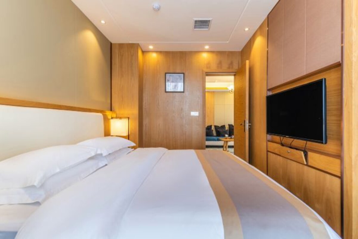 Habitación de hotel con una cama grande, un televisor de pantalla plana montado en la pared y un cabecero de madera.