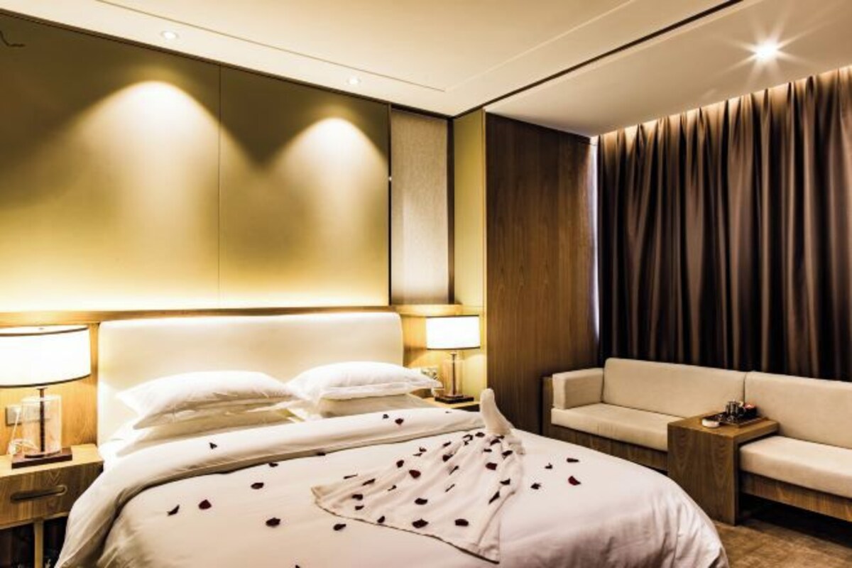 Una habitación de hotel con cama, sofá, mesita de noche y lámpara.