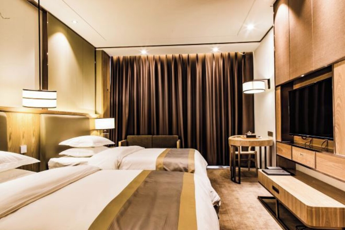 Habitación de hotel con dos camas, un escritorio, una silla, un televisor y un cortinero.