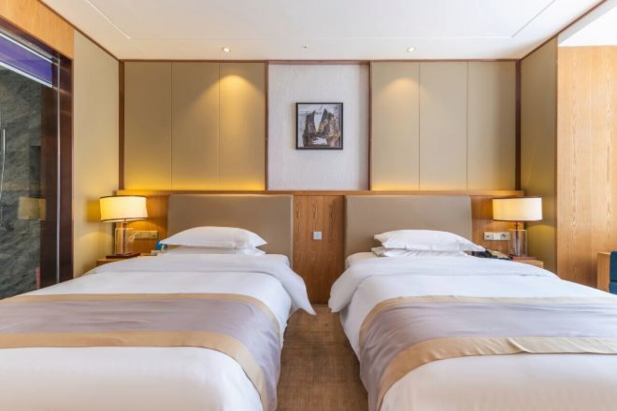 Habitación de hotel con dos camas, cabecero de madera, un cuadro enmarcado en la pared y lámparas de noche.