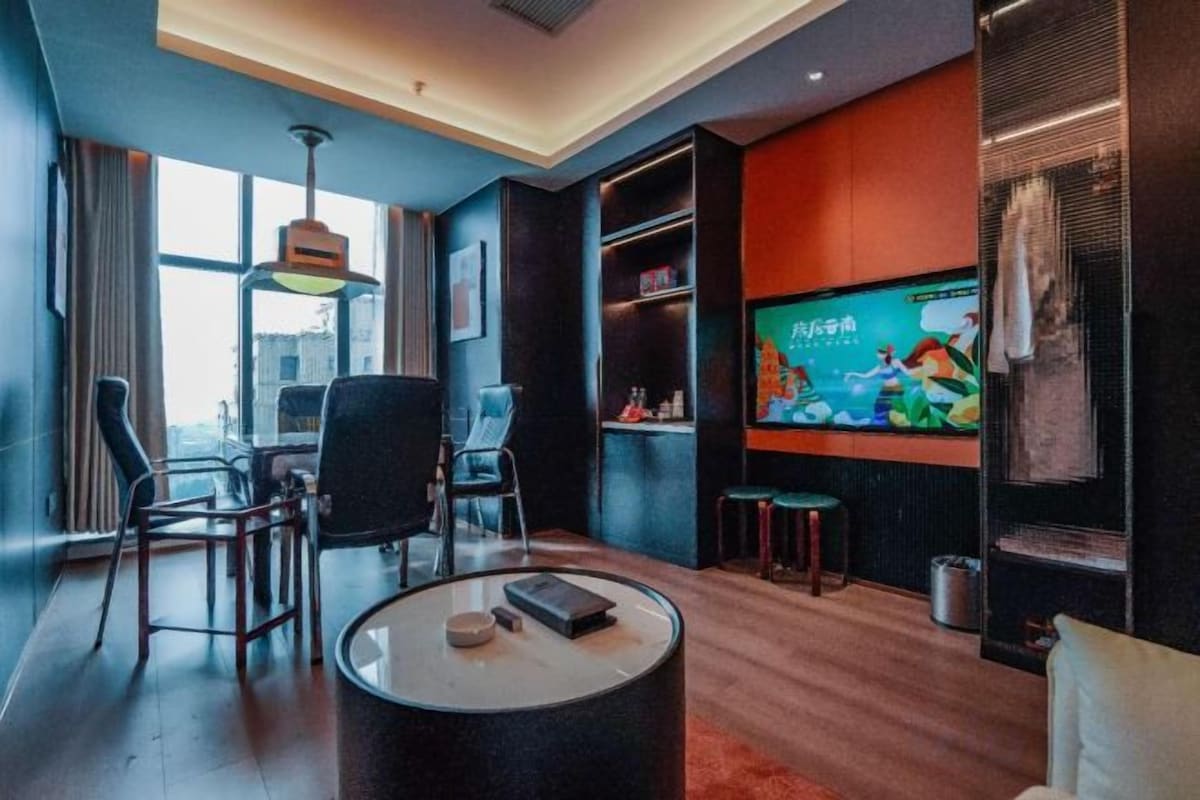 Una habitación de hotel moderna con un televisor grande, asientos cómodos y vistas a la ciudad.