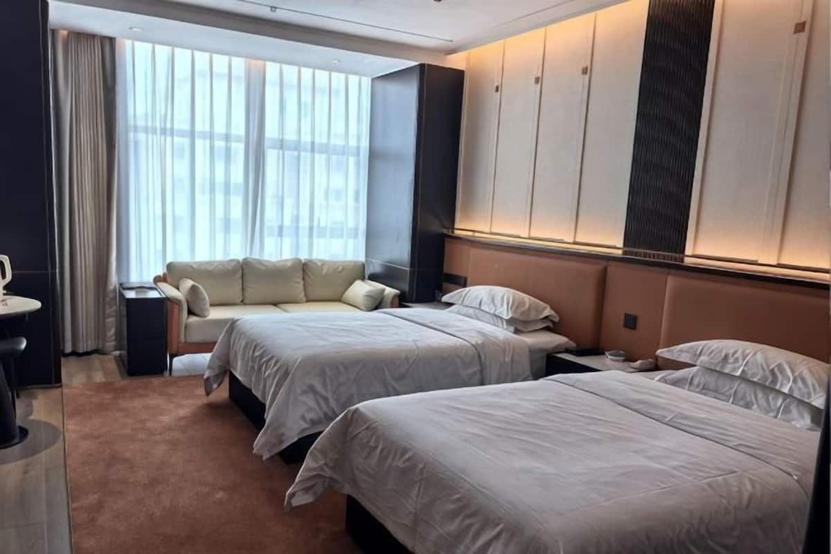 A hotel room with two beds, a sofa, a desk, and a large window with curtains.