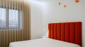 A bedroom with a bed, a nightstand, a lamp, and a window with curtains.