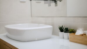 Un évier en céramique blanche, doté d’un robinet moderne, une petite plante en pot et une boîte en bois, le tout posé sur un plan de travail blanc.