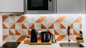 Une cuisine équipée d’un four à micro-ondes, d’une bouilloire et d’une machine à café sur le plan de travail, d’un évier et d’un crédence carrelée.