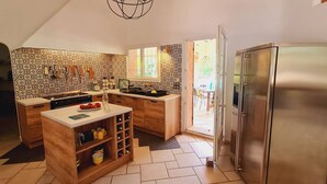 Eine Küche mit einer zentralen Kochinsel, Holzschränken, einem Edelstahlkühlschrank und einer ornamentierten Spritzschutzwand.