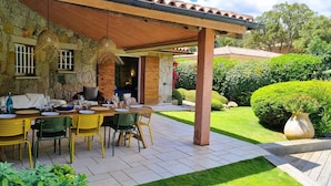 Ein Essbereich im Freien mit Steinmauer, überdachter Terrasse und gepflegtem Garten.