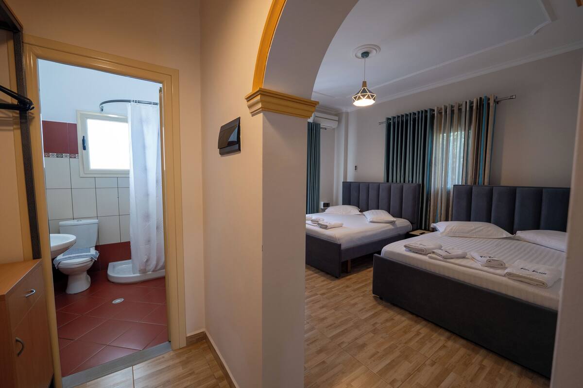 A hotel room with two beds, a bathroom with a shower, and a wooden floor.