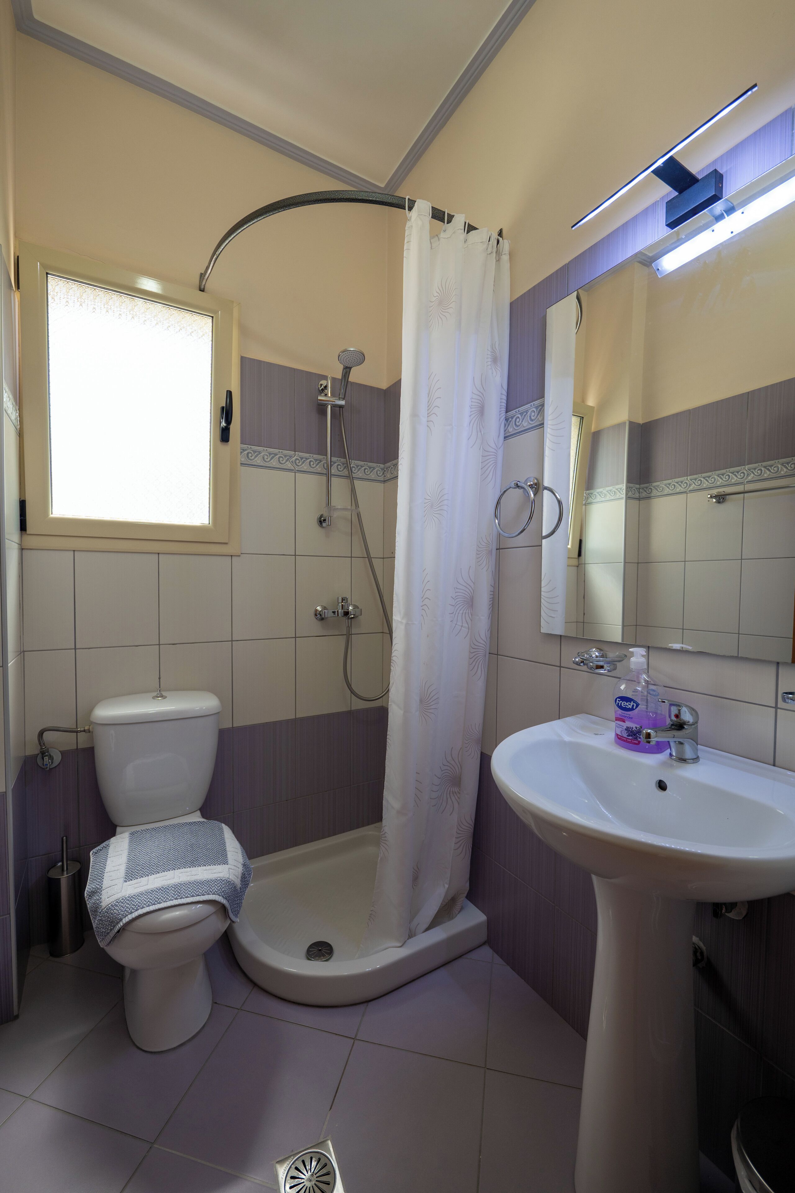 A bathroom with a toilet, shower, sink, and a window.